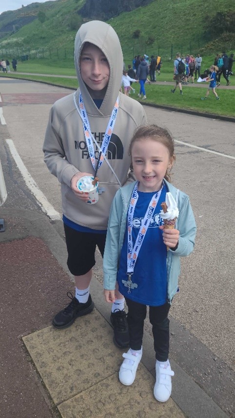 Two children eat ice creams. They're wearing medals and running gear