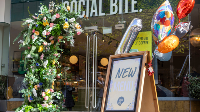 Birthday balloons on a shop A board outside a glass-fronted shop called Social Bite
