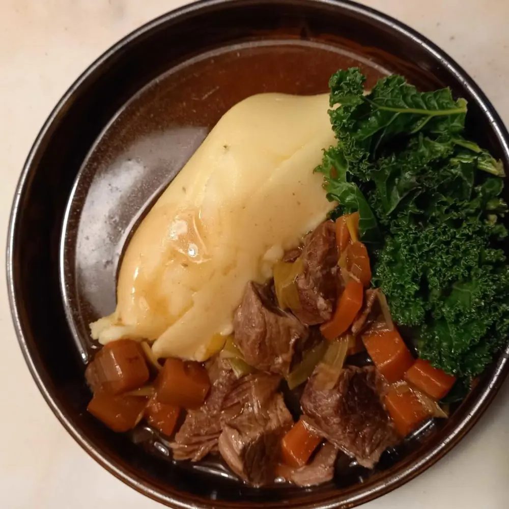 A round bowl with mashed potato, kale, beef stew and gravy