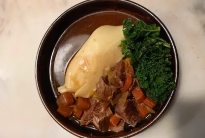 A round bowl with mashed potato, kale, beef stew and gravy