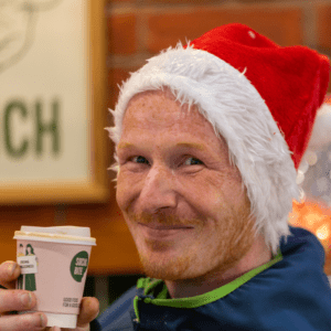 Man in a Santa hat holding a pink takeaway coffee cup