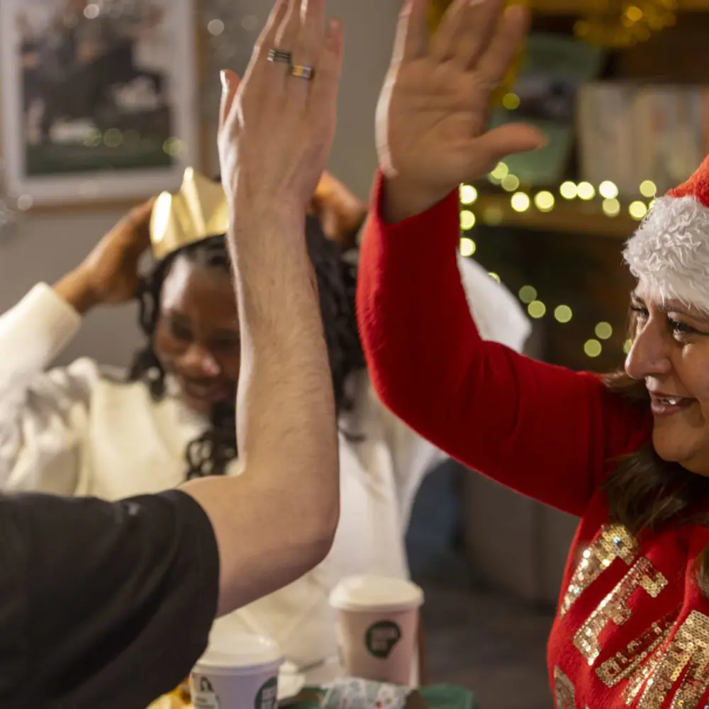 A woman in a Santa hat and a red jumper high-fives a man in a black tshirt