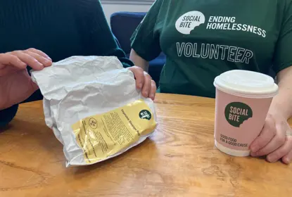 Two people sit together with a coffee. One wears a green tshirt that says volunteer.